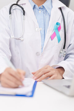 doctor using laptop and report notes on notebook. blue and pink ribbon concept of October male Breast Cancer Awareness month, National Cancer Survivors Month and Pink October Healthcare