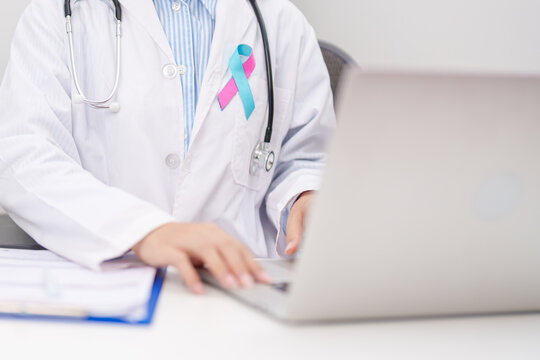 doctor using laptop and report notes on notebook. blue and pink ribbon concept of October male Breast Cancer Awareness month, National Cancer Survivors Month and Pink October Healthcare