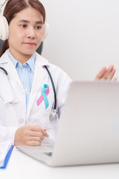 doctor using laptop for telehealth, online consultation and meeting about blue and pink ribbon concept of October male Breast Cancer Awareness month, National Cancer Survivors Month