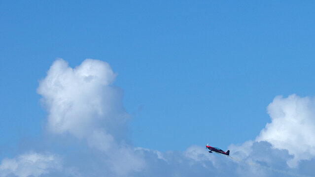 Aerobatic Stunt Plane Flying Through Blue Sky and White Clouds