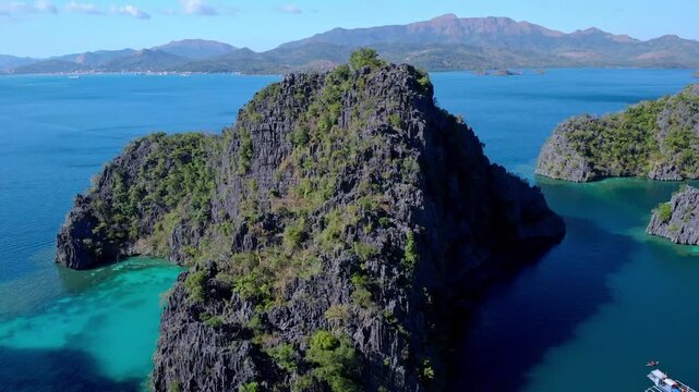 Aerial view of limestone cliffs rising from turquoise waters with traditional outrigger boats in Palawan, Mimaropa, Philippines.