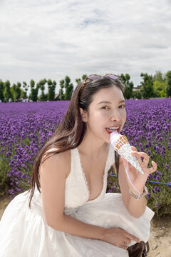 ​Woman holding a lavender soft-serve ice cream cone with  colorful flower fields background.