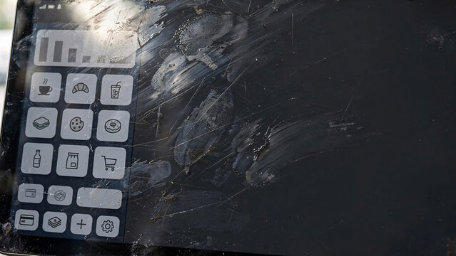 A damaged point-of-sale terminal shows scratches and dirt on its screen, with a keypad featuring various icons.