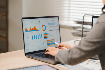 Businesswoman analyzing financial performance charts and dashboard data on laptop screen at office desk
