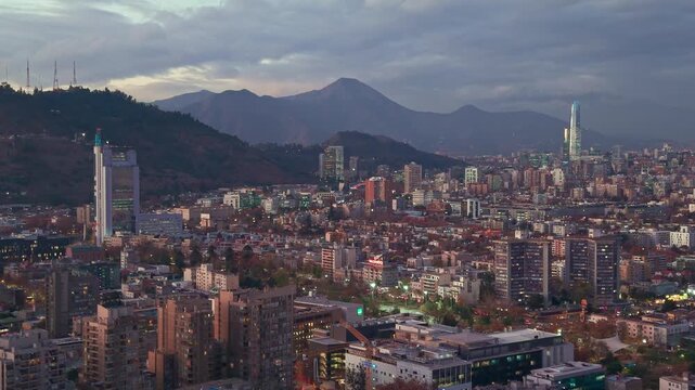 Aerial view of the Santiago city skyline with modern buildings and residential areas set against the Andes mountains under a cloudy dusk sky in Santiago, Santiago Metropolitan, Chile.