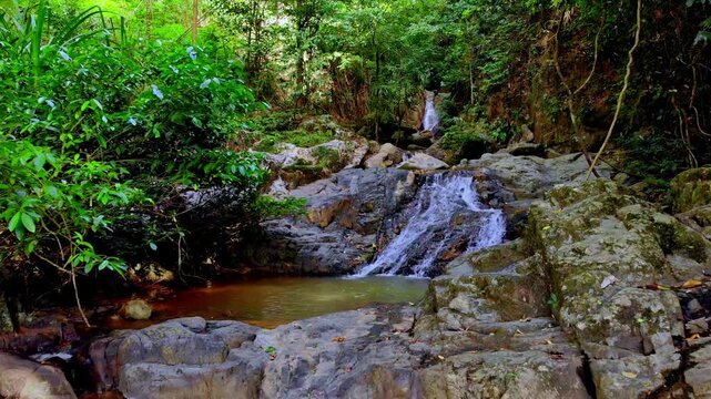 Aerial view of a waterfall cascading over rocks into a clear pool surrounded by dense tropical forest in Palawan, Mimaropa, Philippines.