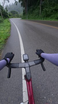 View from a cyclist's perspective on a quiet road, flanked by greenery and misty hills, capturing the essence of outdoor adventure.