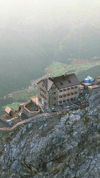 Aerial view of Payer Hutte perched on a rocky ridge of Ortler Mountain with steep alpine slopes and distant valley views in Sulden, Trentino-Alto Adige, Italy.