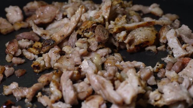 Chunks of meat sizzling and browning in a dark pan. The pieces of meat feature a golden-brown sear, a juicy texture, and an appetizing appearance. 