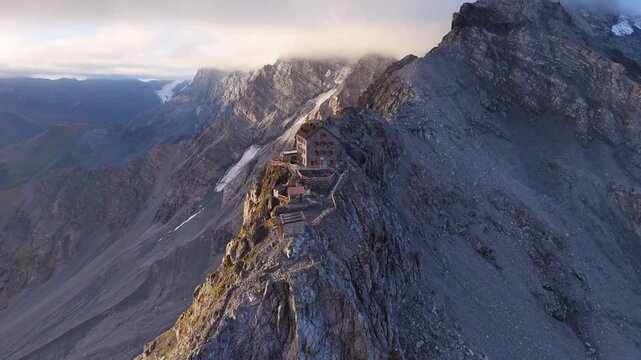 Aerial view of Payer Hutte perched on a rocky ridge of Ortler Mountain, surrounded by steep alpine slopes and glaciers in Sulden, Trentino-Alto Adige, Italy.