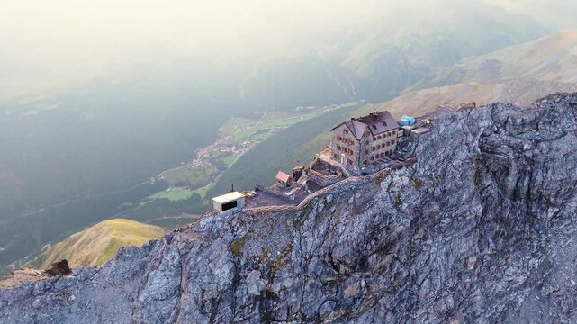 Aerial view of Payer Hutte perched on the rugged rocky ridge of Ortler Mountain at sunset, with dramatic mountain peaks in the background in Sulden, Trentino-Alto Adige, Italy.