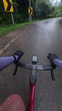 Cyclist Riding on Wet Road in Rainy Weather with Lush Greenery and Passing Car in Background
