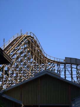 Wooden roller coaster track climbing up a steep hill against a clear sky