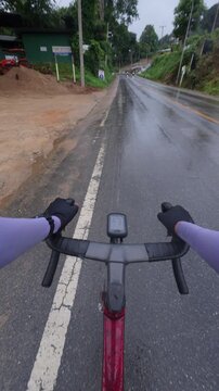 Cyclist's Perspective on a Rainy Road with Lush Greenery and Overcast Sky Captured from Handlebar View