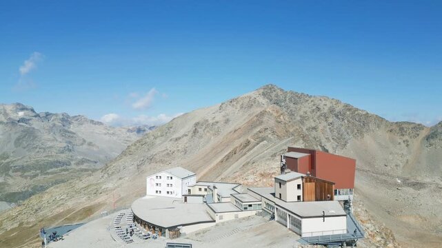 Aerial view of the Diavolezza mountain station with the rugged Piz Bernina massif in the background under a clear blue sky in Pontresina, Grisons, Switzerland.