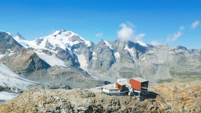Aerial view of the Diavolezza mountain station with the snowy peaks of Piz Bernina in the background under a clear blue sky in Pontresina, Grisons, Switzerland.