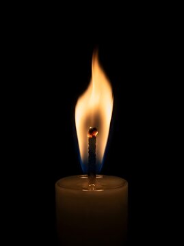 A single glowing candle wick burns brightly in the dark night casting warm light across the room atmosphere while providing comfort during quiet moments of reflection and peaceful meditation