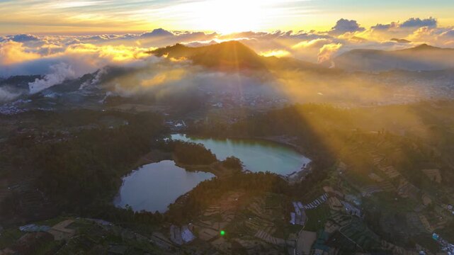 Aerial view of Dieng Plateau with its volcanic lakes and terraced fields illuminated by golden sunrise light in Indonesia.