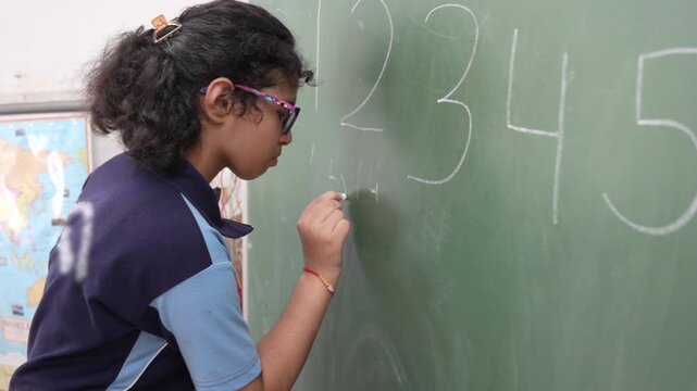 Indian schoolgirl with special educational needs practice writing on  greenboard in classroom,  inclusive education learning support, childhood development, empowerment, and equal opportunities.