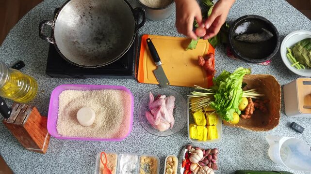 Overhead view of chef cutting galangal root on orange board with various cooking ingredients around
