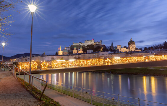 Salzburg Old Town with Hohensalzburg Fortress and an illuminated bridge reflected in the Salzach River at blue hour, Austria.