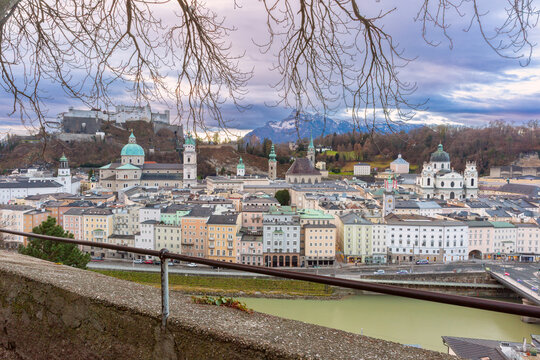 Wide panoramic view of Salzburg Old Town along the Salzach River with historic architecture and Hohensalzburg Fortress at dusk, Austria.
