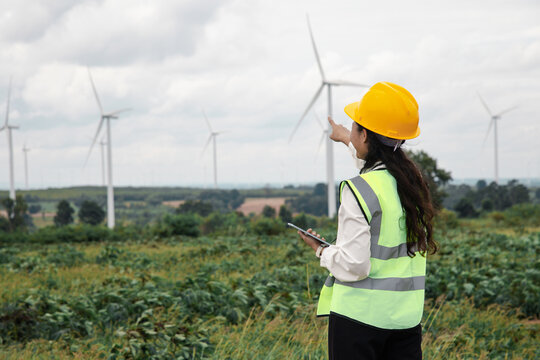 Engineer using a digital tablet at a green wind turbine farm to inspect renewable energy operations.