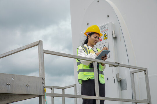 Engineer using a digital tablet at a green wind turbine farm to inspect renewable energy operations.