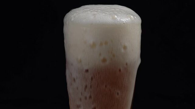 Closeup hoppy unfiltered beer foaming in glass. Foam alcohol beverage flowing down clean goblet on black background. 