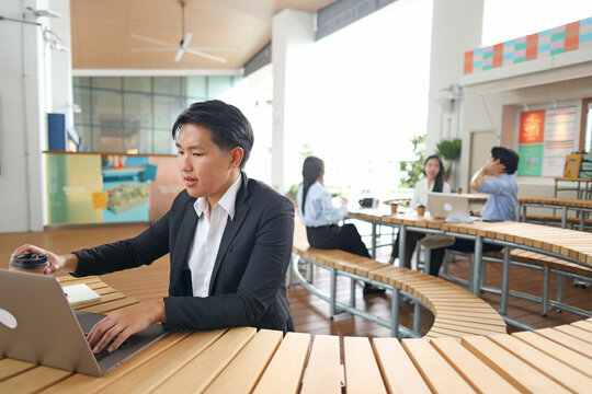 Young Asian Businessman Working on Laptop in Modern Coworking Space