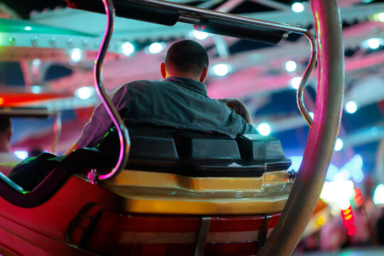 Father And Daughter Enjoying Amusement Park Ride on Holidays. Man in denim shirt from behind riding a colorful carousel with his little daughter