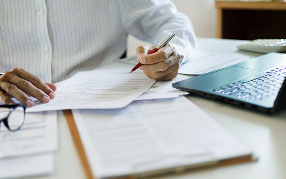 close up shot, asian businessman reviewing document at office working on laptop. professional lawyer reading and checking business documents and contract before giving advice to customers