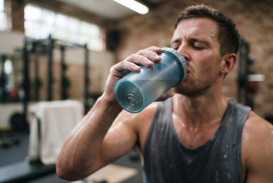 Close-up of a sweaty man drinking water from a shaker bottle during a workout in a gym.