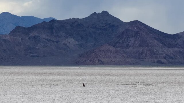 Aerial view of Bonneville Salt Flats with two people standing on the vast white salt crust under a dramatic mountain range in Tooele County, Utah, United States.