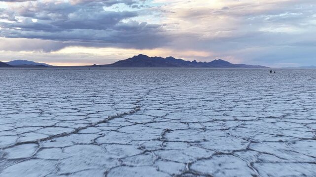 Aerial view of Bonneville Salt Flats with vast salt crust patterns and distant mountains under a dramatic cloudy sky in Tooele County, Utah, United States.