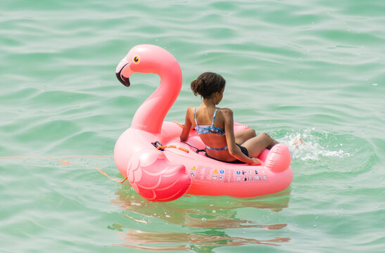 Person in a two-piece swimsuit sitting on an inflatable water toy surrounded by sparkling sea water during a relaxing holiday in the Mediterranean region