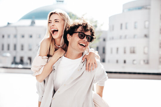 Young smiling beautiful woman and her handsome boyfriend in casual summer clothes. Happy cheerful family. Couple posing in street at sunny day. Female sits at his back. piggyback riding