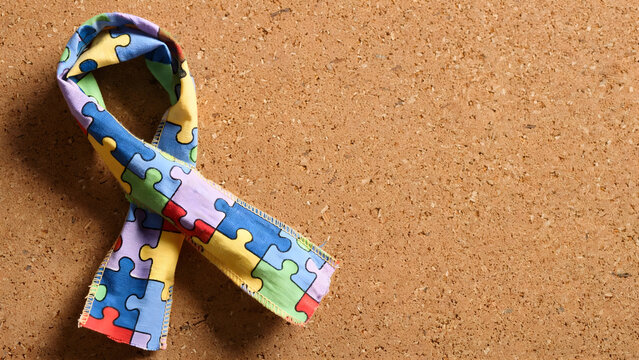 Multicolor puzzle ribbon symbol on corkboard background for awareness message