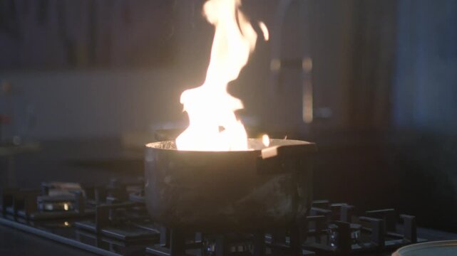 Flame Bursting Out of a Cooking Pot on a Gas Stove in a Dark Kitchen, Dangerous Kitchen Fire Accident Close Up, Cooking Oil Catching Fire Emergency Concept, Stovetop Flambe Blaze Warning Footage