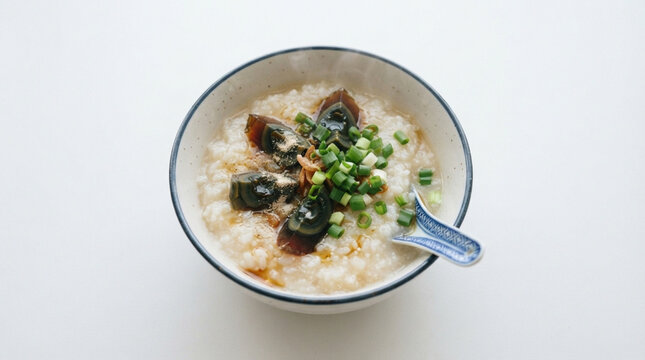Traditional Asian rice porridge congee served in a porcelain bowl, topped with century egg slices, chopped green onions, and seasonings.