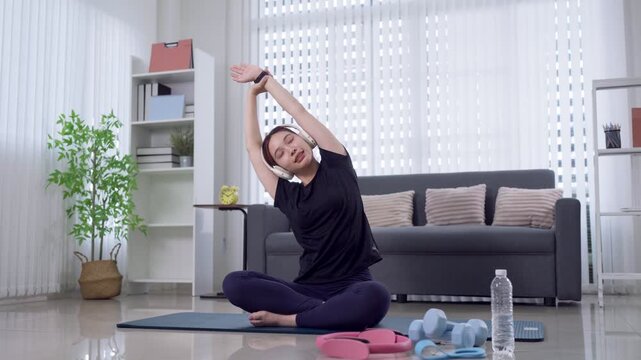 Young Asian woman performing side stretch yoga pose on mat in bright modern living room at home