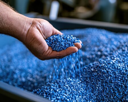 Hand holding a handful of blue plastic polymer pellets for industrial manufacturing and material processing