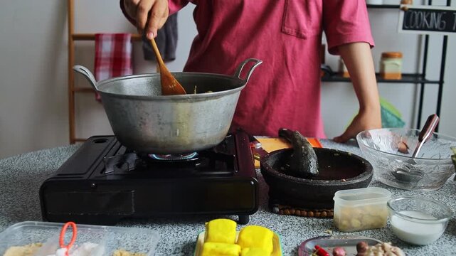 Homechef stirring simmering chicken curry with wooden spatula broth in pot on gas stove