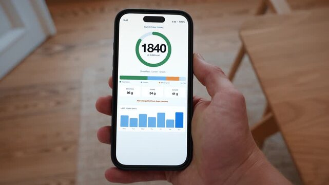 A nutrition app shows the day in calories with protein, carbohydrate and fat split out. Point of view shot with the phone held in the hand. Useful for promoting a healthy lifestyle.