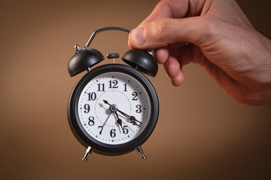 Alarm clock in hand on brown background. Time management concept.