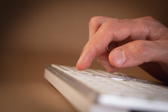 Close up of a male hand typing on a computer keyboard on a brown background