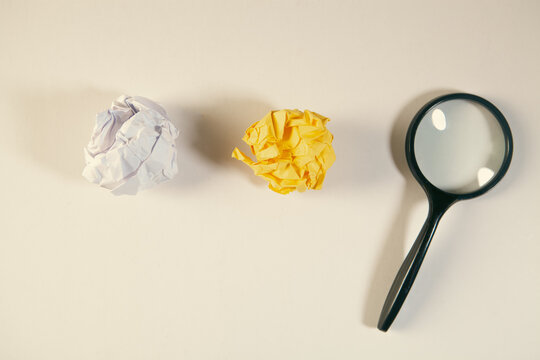 Crumpled paper ball and magnifying glass on white background.