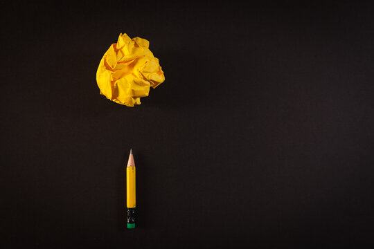 Yellow crumpled paper ball and yellow pencil on black background with copy space