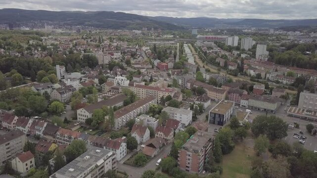 Drone crosses a residential quarter with Messe Basel towers and canal visible behind.