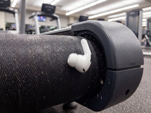 Wireless earbud lost on treadmill belt in a gym, symbolizing workout mishap or technical issue.
